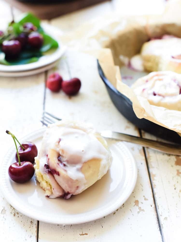Cherry Roll with icing and fresh cherries on a white plate.
