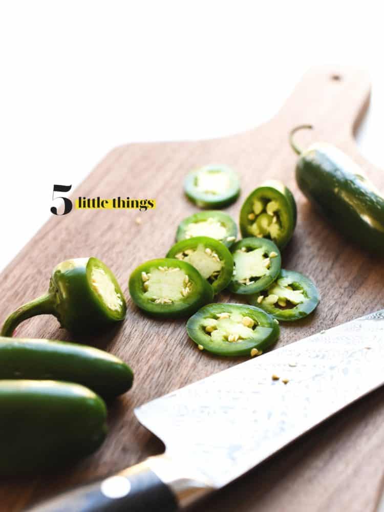 Sliced jalapenos on a wooden cutting board with a chef's knife.