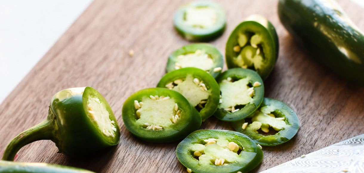 Sliced jalapenos on a wooden cutting board with a chef's knife.