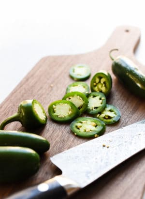 Sliced jalapenos on a wooden cutting board with a chef's knife.
