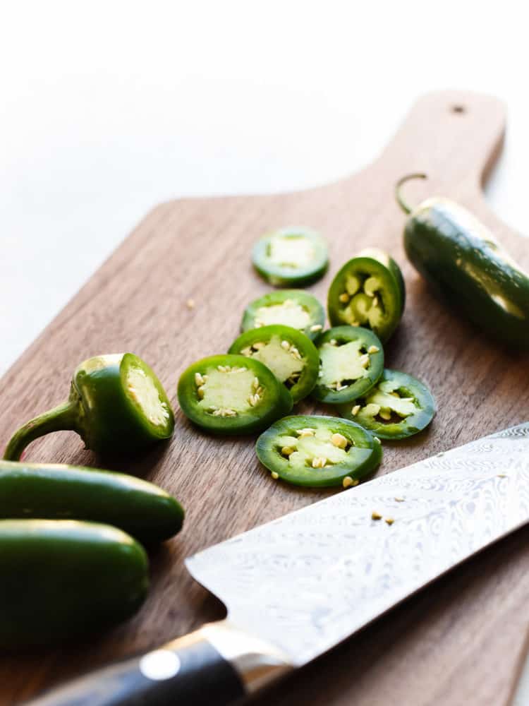 Sliced jalapenos on a wooden cutting board with a chef's knife.