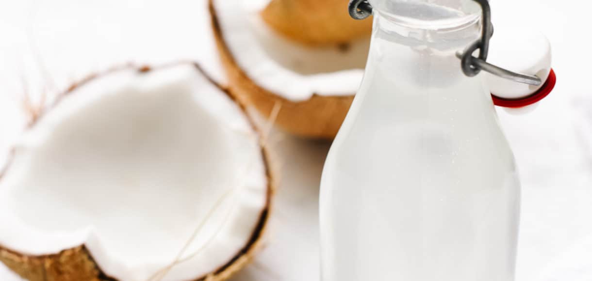 Glass bottle of homemade coconut water and large pieces of coconut