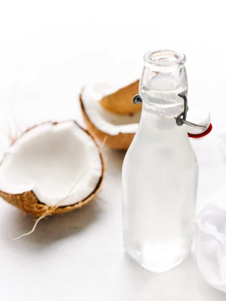 Glass bottle of homemade coconut water and large pieces of coconut