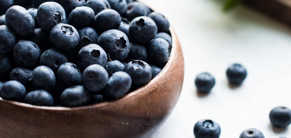 Wooden bowl of blueberries with blueberries on the counter.