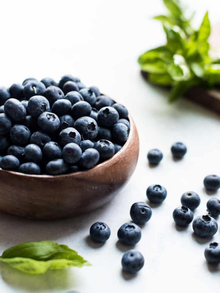 Wooden bowl of blueberries with blueberries on the counter.