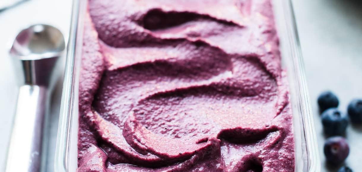 Blueberry Açaí Frozen Yogurt in a glass loaf pan with ice cream scoop and blueberries for garnish.