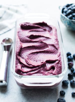 Blueberry Açaí Frozen Yogurt in a glass loaf pan with ice cream scoop and blueberries for garnish.
