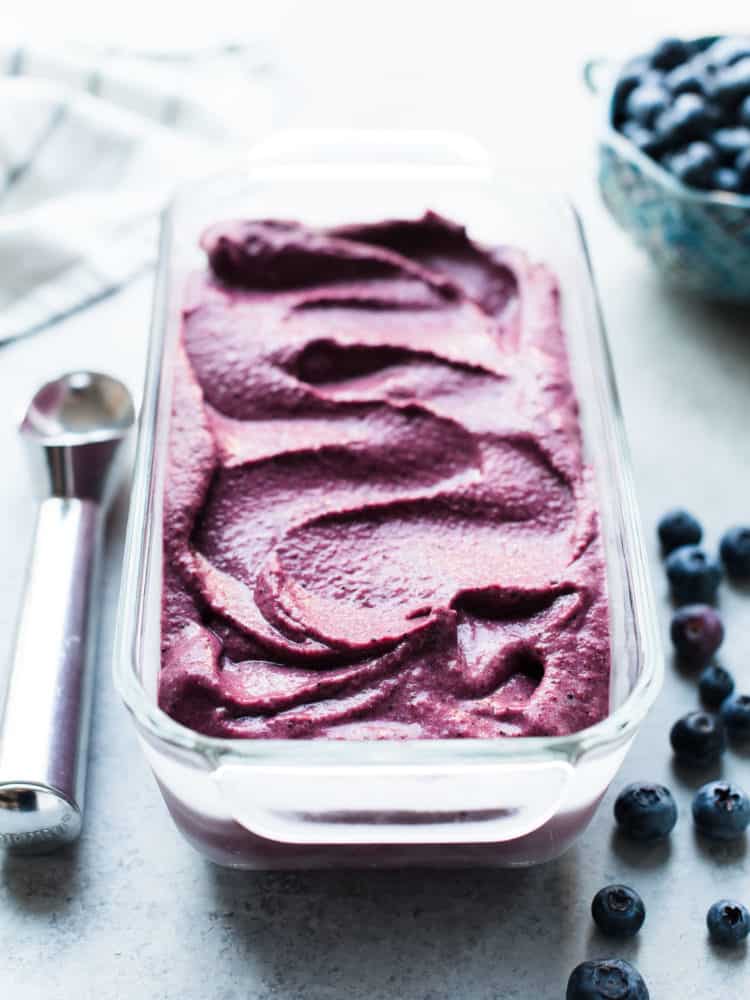 Blueberry Açaí Frozen Yogurt in a glass loaf pan with ice cream scoop and blueberries for garnish.