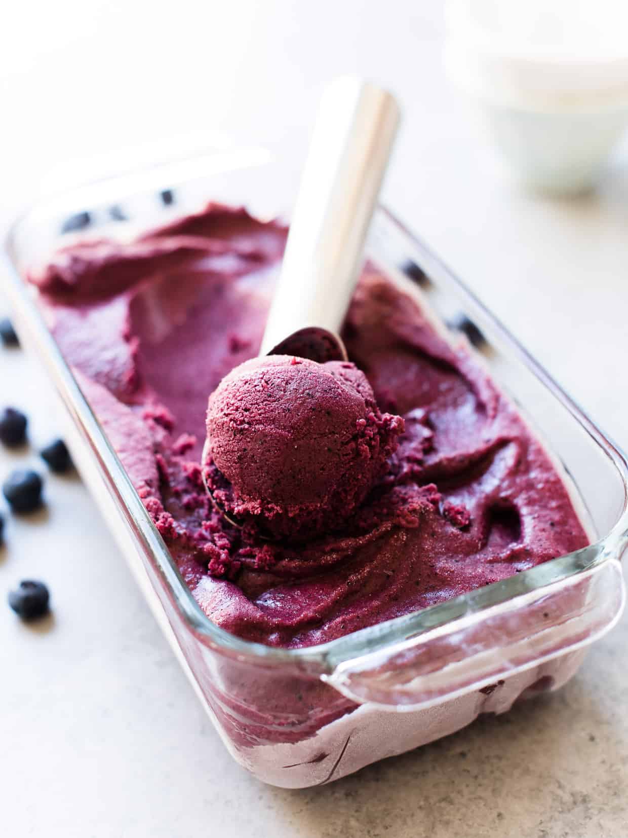 Blueberry Açaí Frozen Yogurt in a glass loaf pan with ice cream scoop and blueberries for garnish.