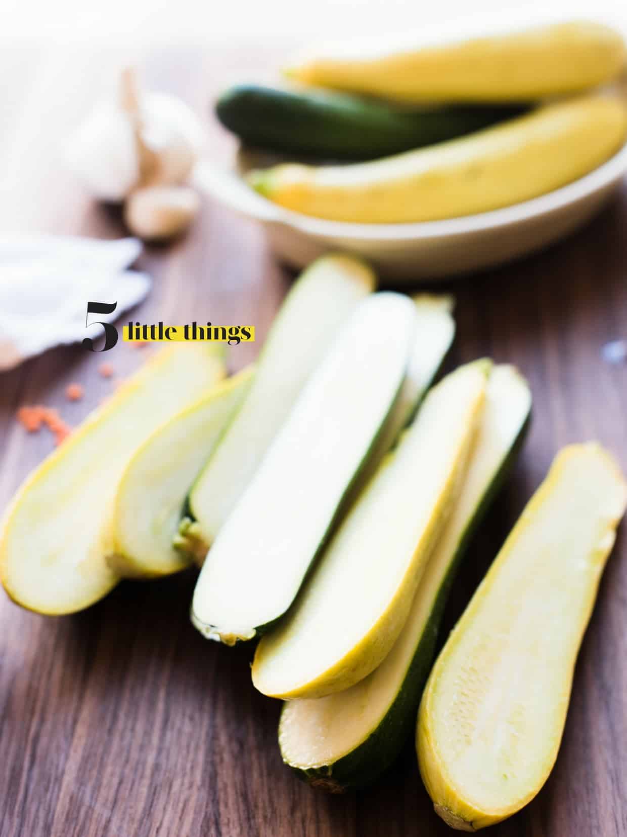 Zucchini and summer squash halved lengthwise on a wooden cutting board.