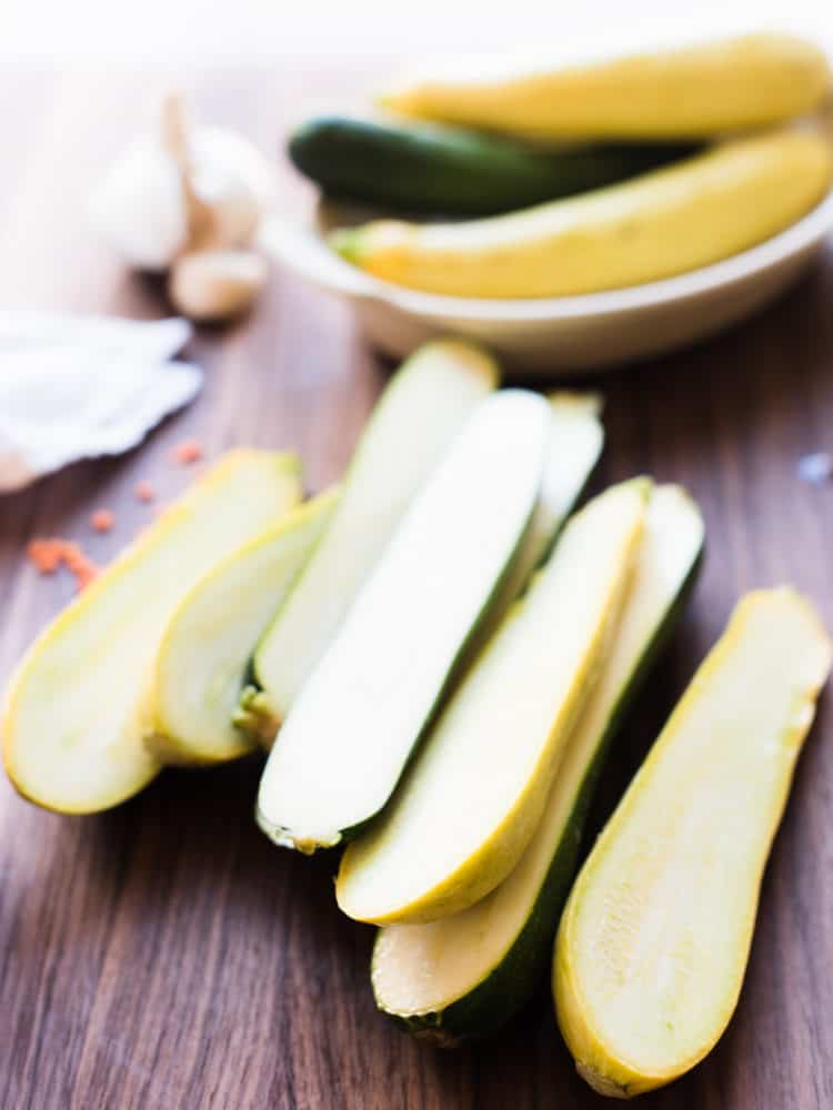 Zucchini and summer squash halved lengthwise on a wooden cutting board.