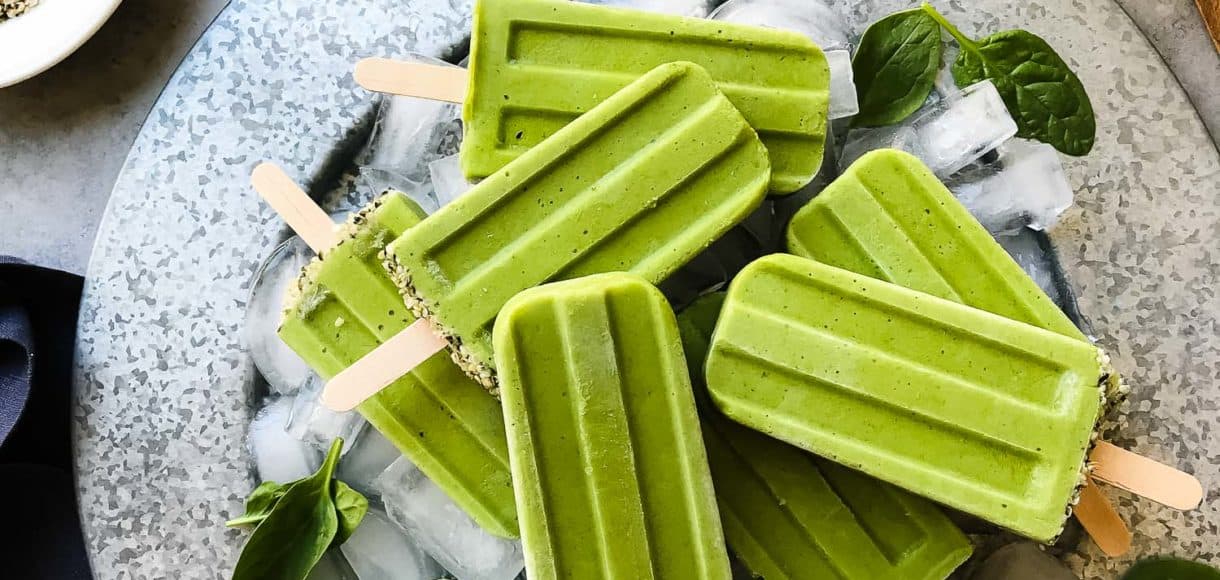 Green Smoothie Popsicles on a platter with ice cubes and fresh baby spinach leaves for garnish.