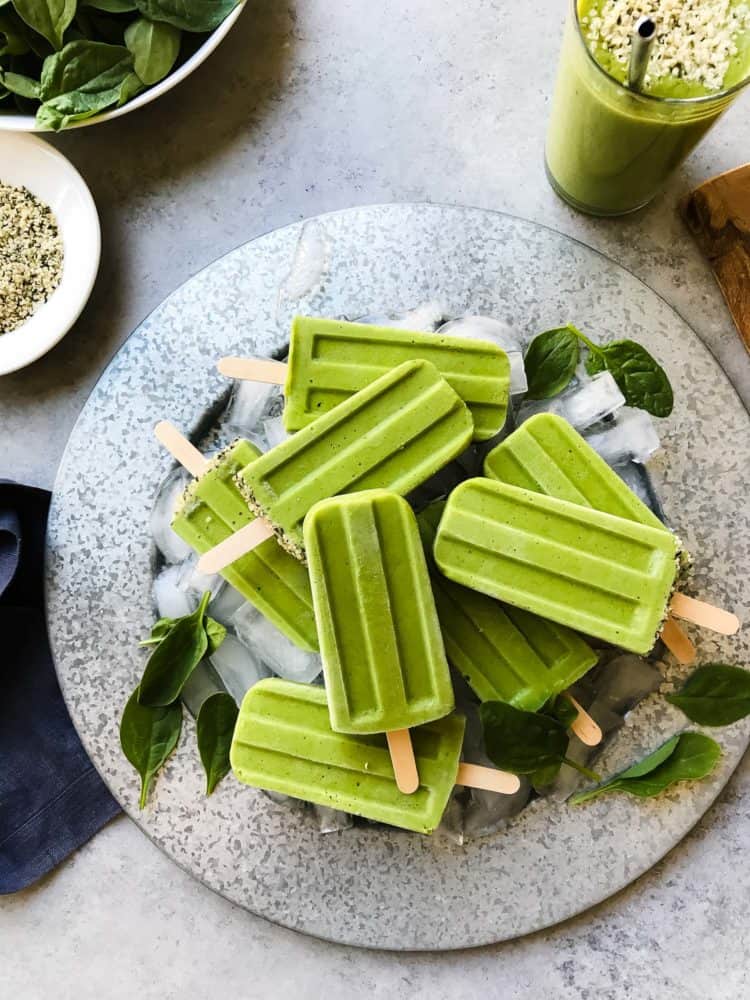 Green Smoothie Popsicles on a platter with ice cubes and fresh baby spinach leaves for garnish.