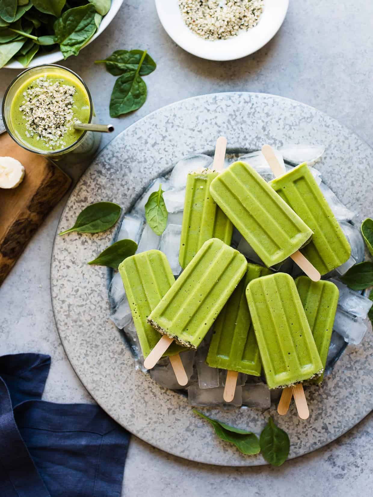 Green Smoothie Popsicles on a platter with ice cubes and fresh baby spinach leaves for garnish.