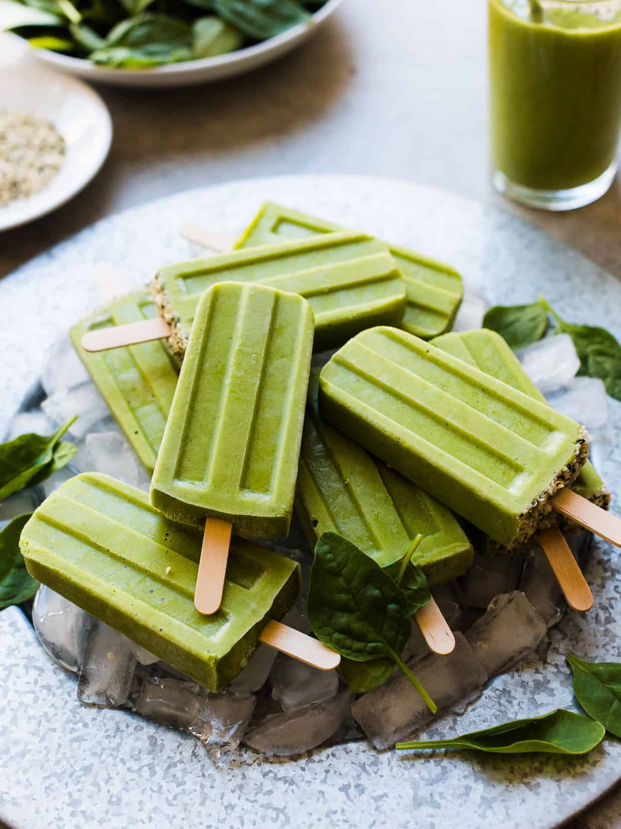 Green Smoothie Popsicles on a platter with ice cubes and fresh baby spinach leaves for garnish.