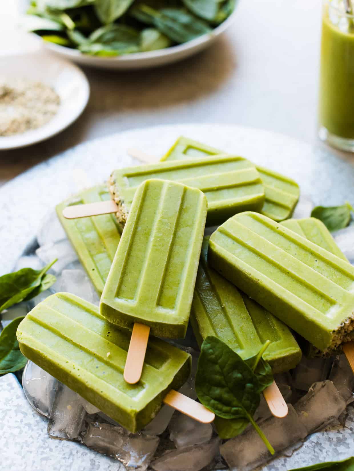 Green Smoothie Popsicles on a platter with ice cubes and fresh baby spinach leaves for garnish.