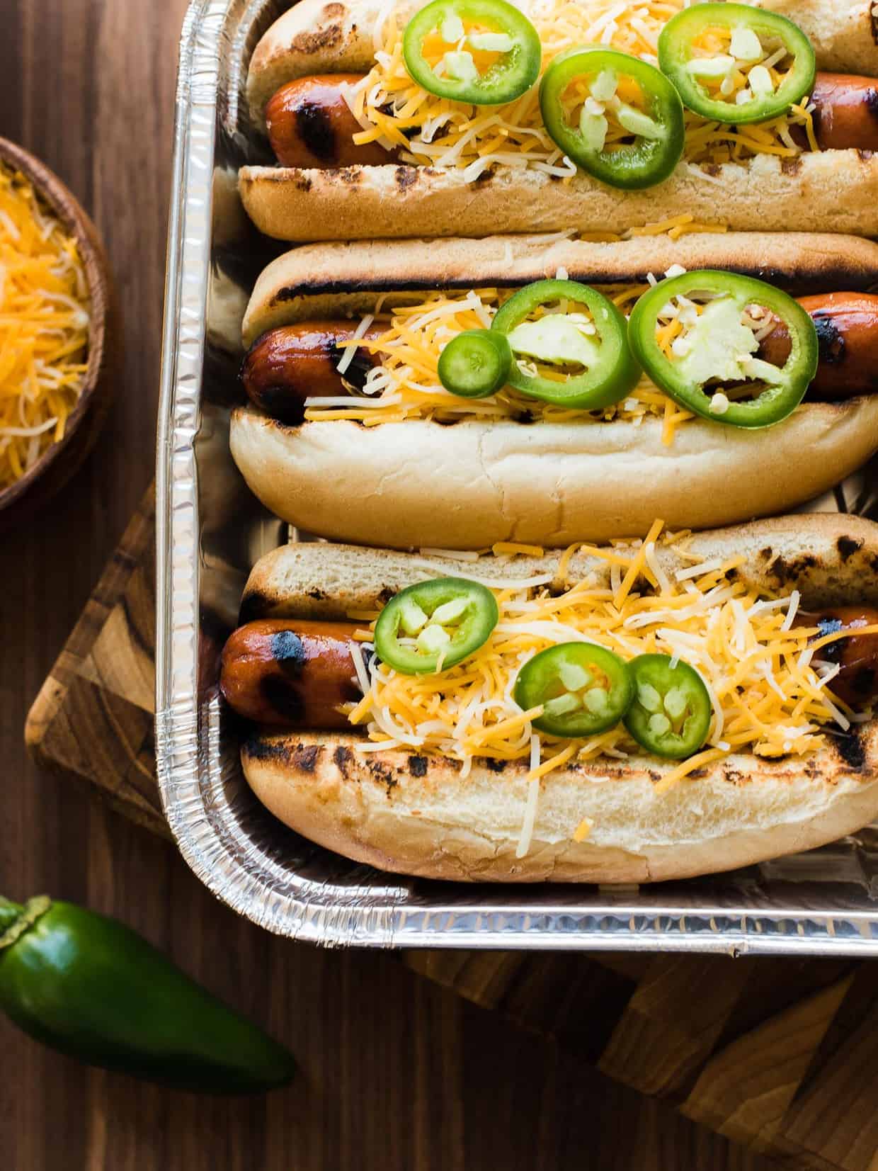 Sriracha Hot Dogs in buns with cheese and jalapeños.