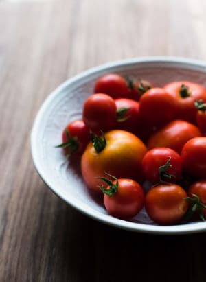A white bowl filled with red tomatoes.