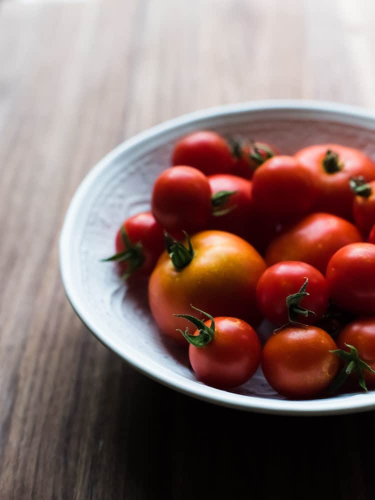 A white bowl filled with red tomatoes.