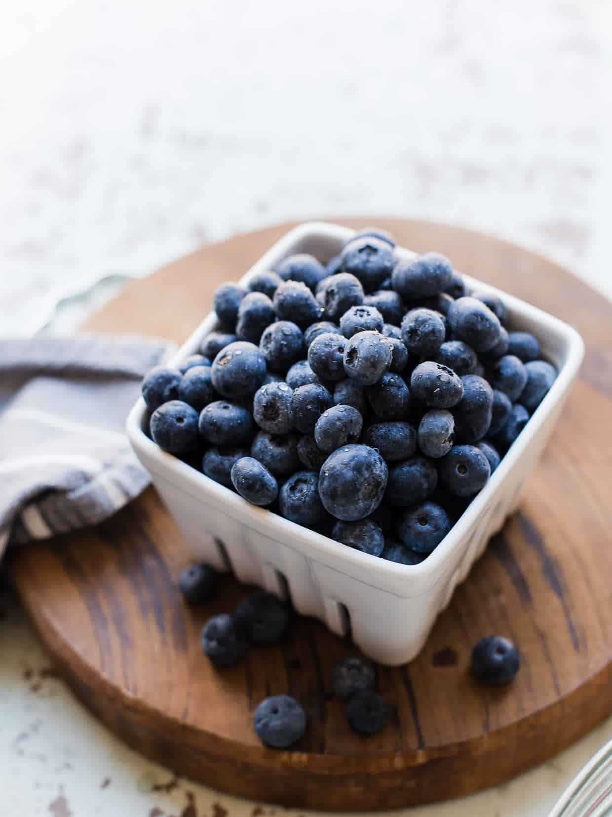 Fresh blueberries in a white basket on a wooden cutting board.