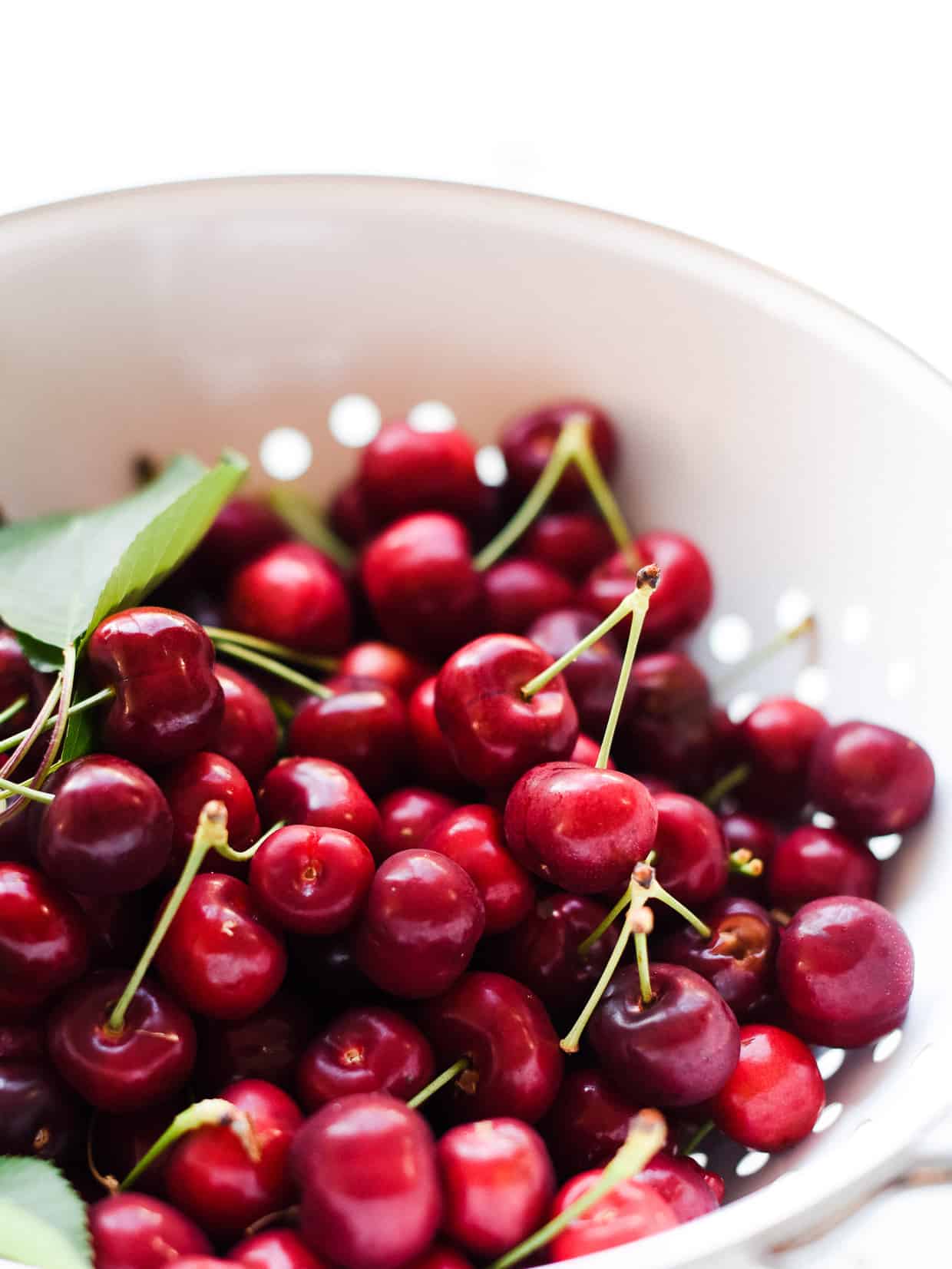 Fresh cherries with stems in a white colander.