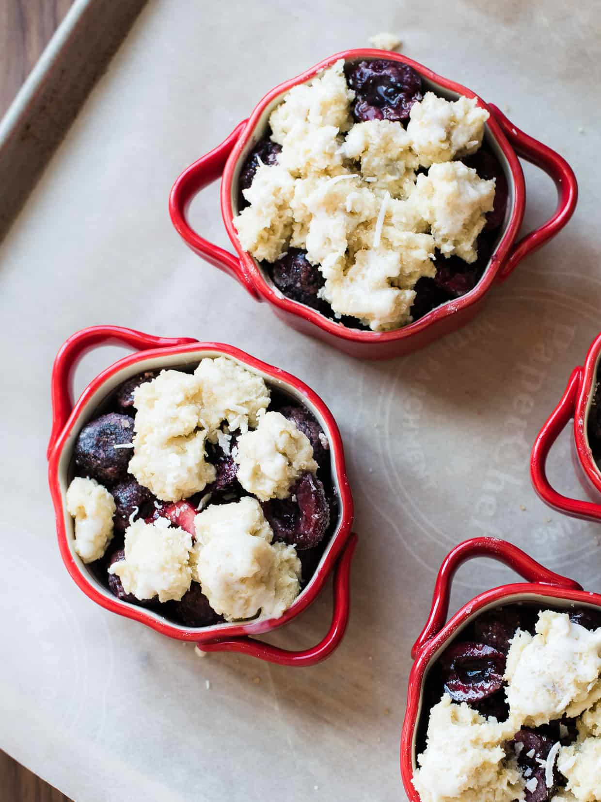 Individual size coconut cherry cobblers ready to bake in red ramekins.