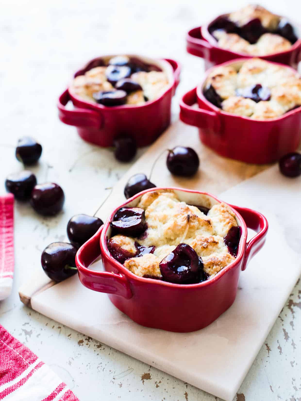 Individual size coconut cherry cobblers served in red ramekins with vanilla ice cream.