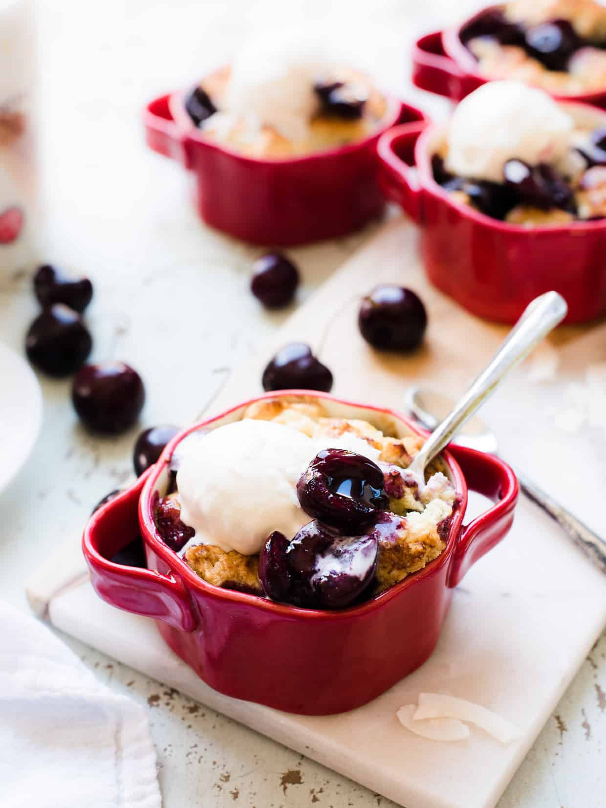 Individual size coconut cherry cobblers served in red ramekins with vanilla ice cream.