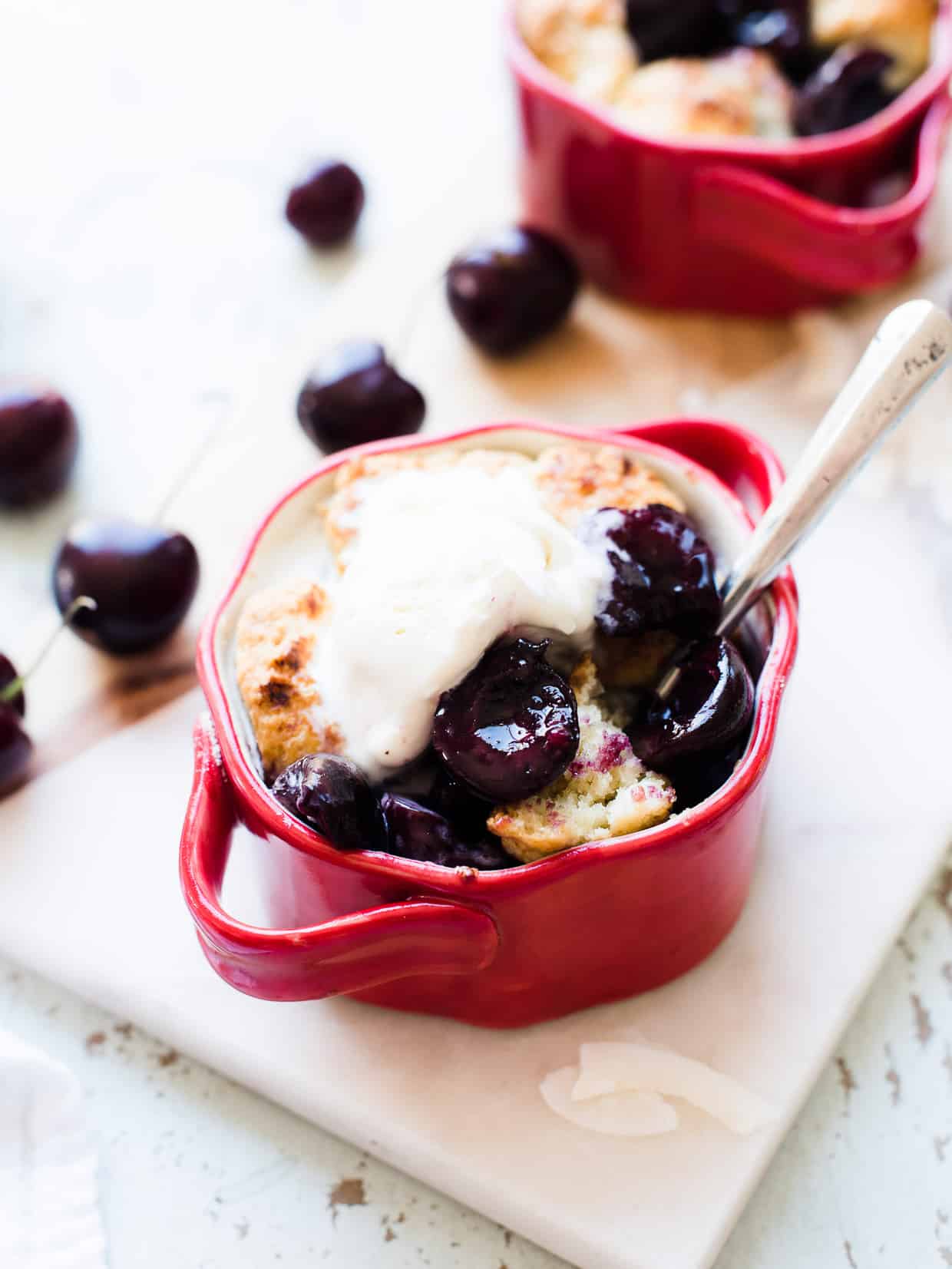 Individual size coconut cherry cobblers served in red ramekins with vanilla ice cream.