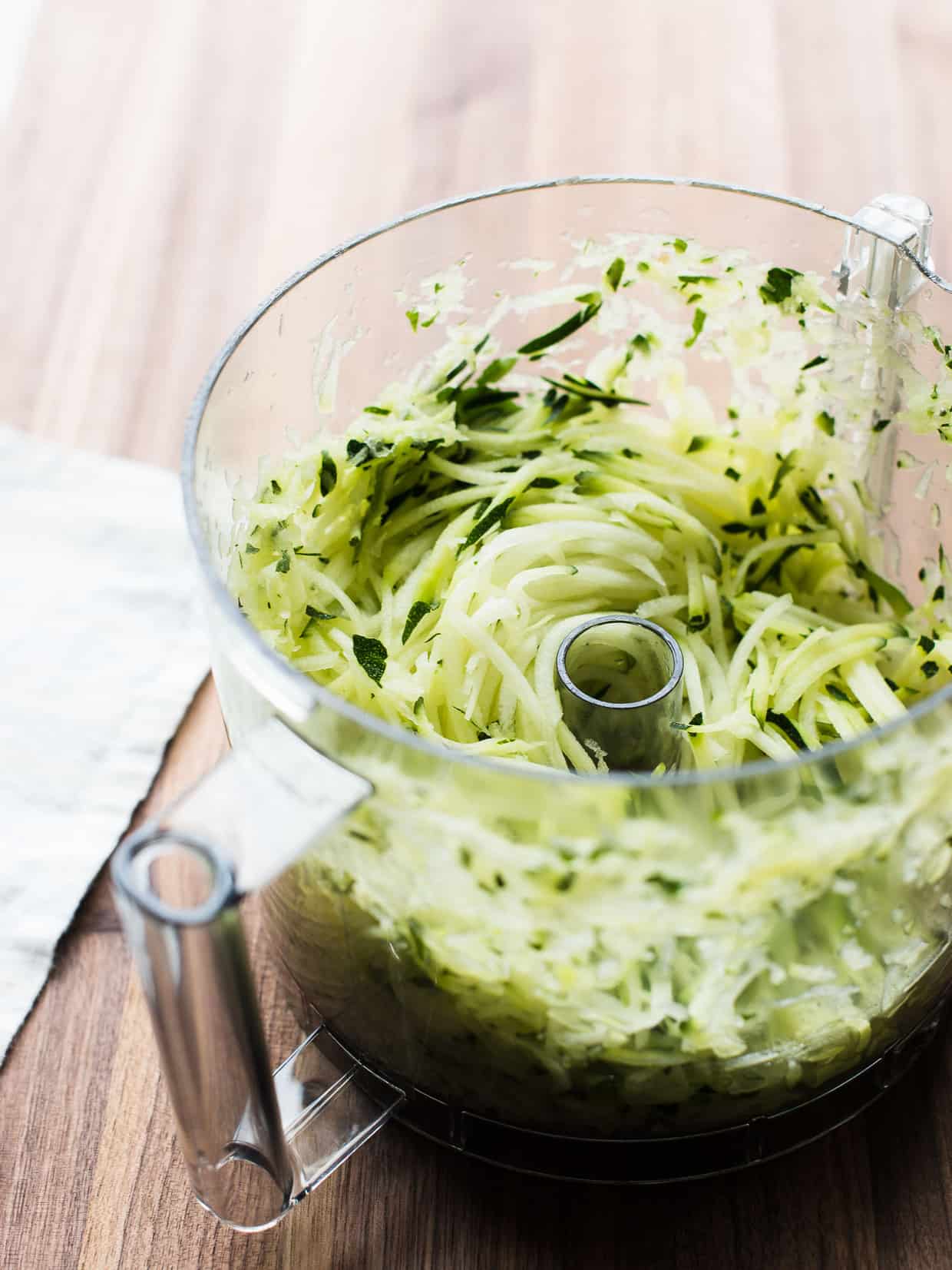 Grated zucchini in a food processor bowl for Coconut Zucchini Coffee Cake.