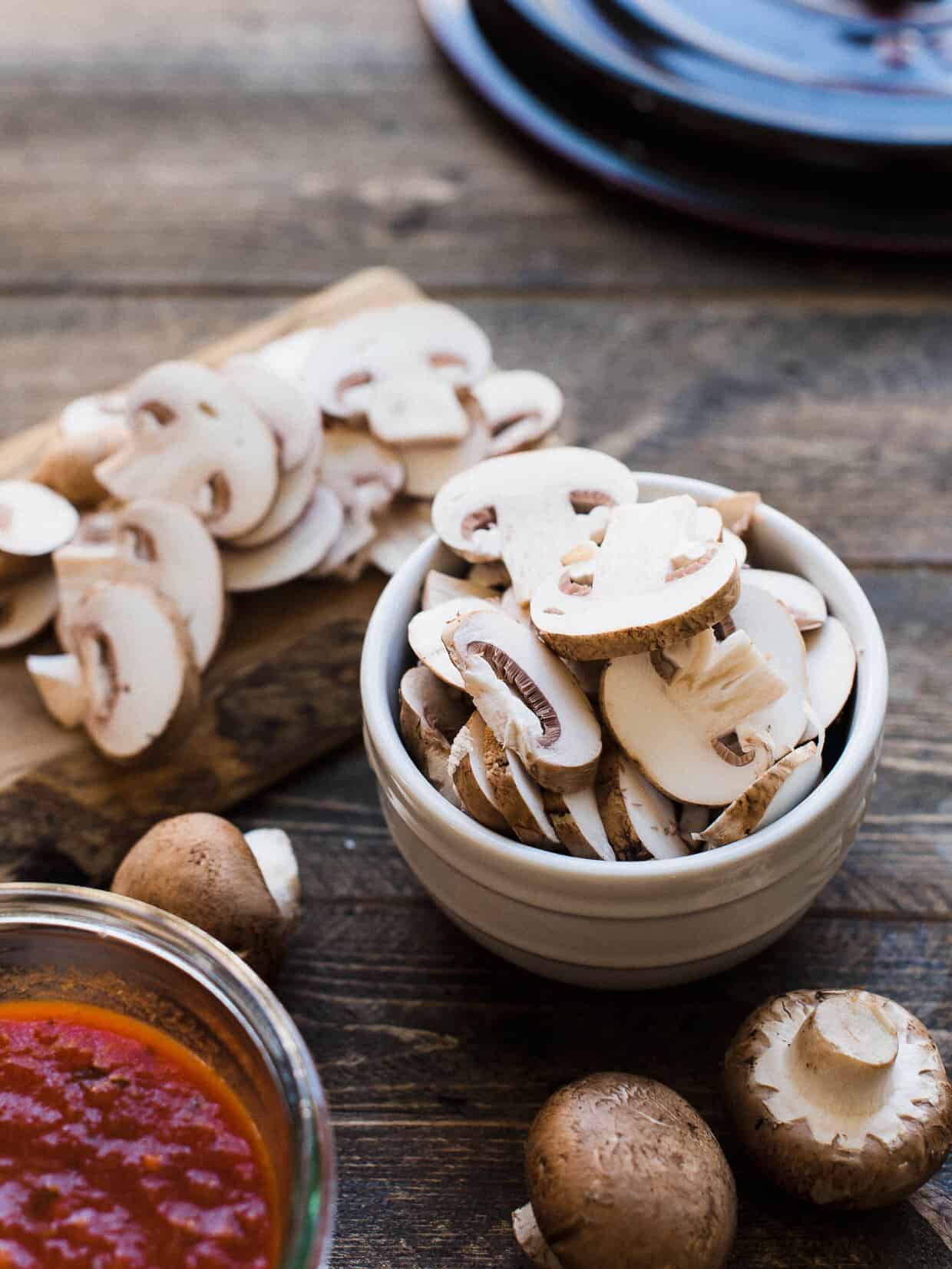 Sliced mushrooms in a white bowl on a wooden surface.