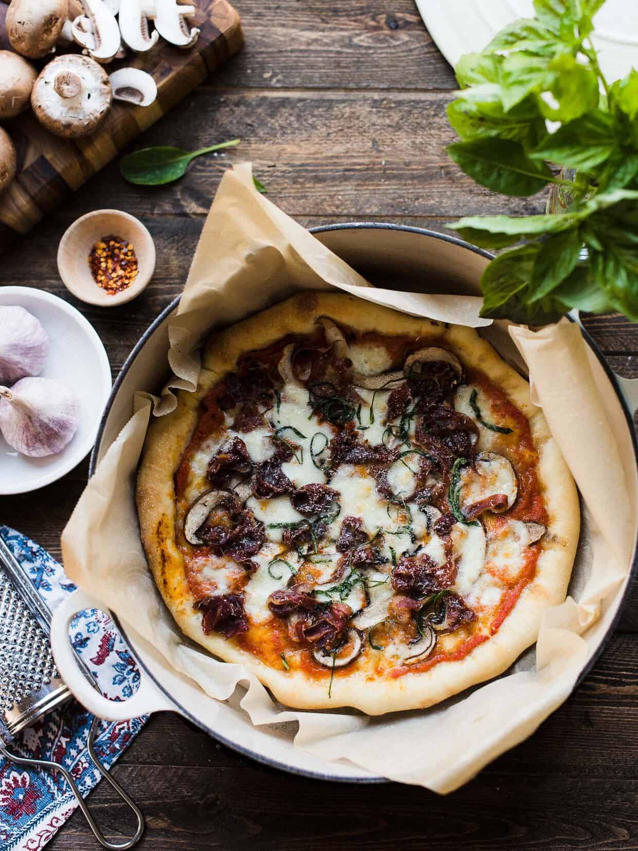 Dutch Oven Pizza baked in a Dutch oven lined with parchment paper on a wooden surface.