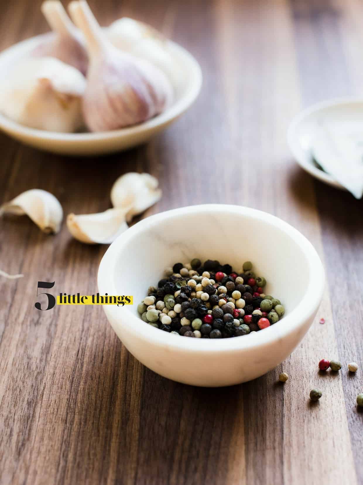 Multi-colored peppercorns in a small white marble bowl with garlic in the background.