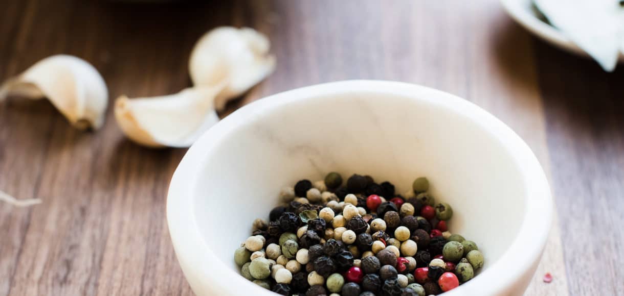 Multi-colored peppercorns in a small white marble bowl with garlic in the background.