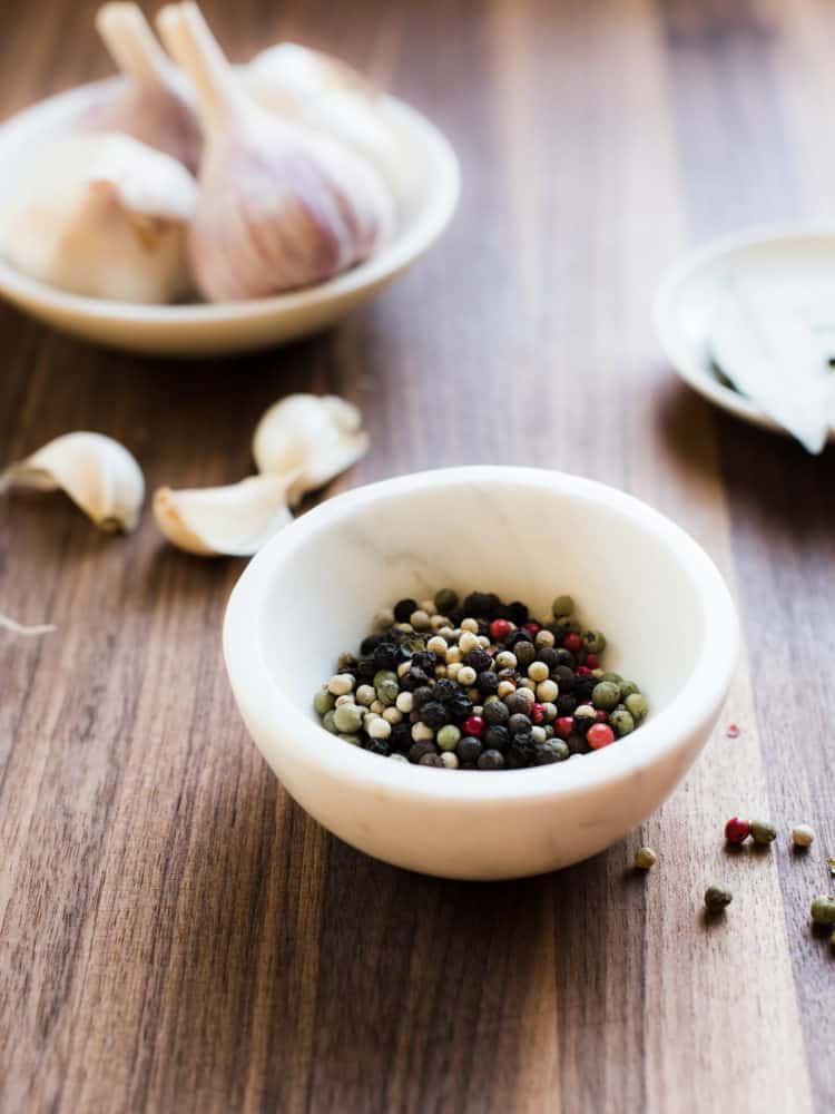 Multi-colored peppercorns in a small white marble bowl with garlic in the background.