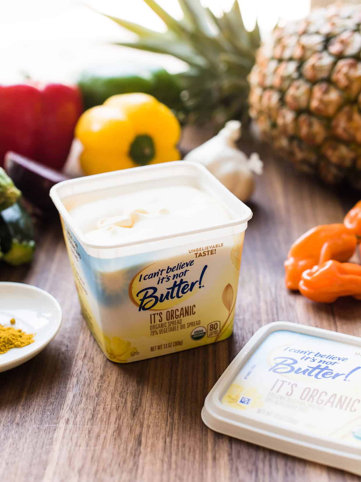 An open container of I Can't Believe It's Not Butter with pineapple, habenero, and peppers in the background.