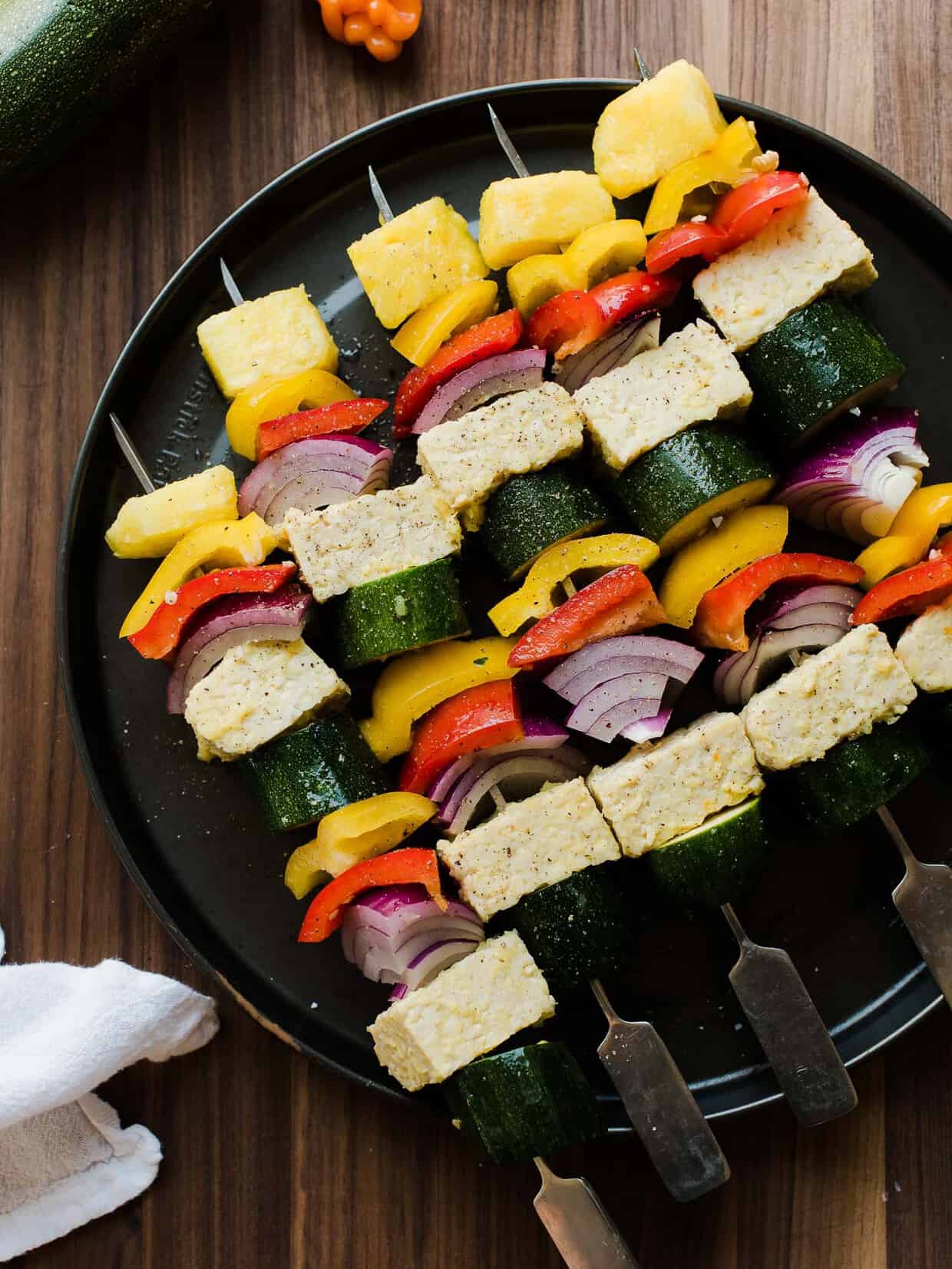 Grilled vegetable skewers with pineapple on a black plate.