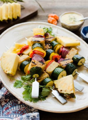 Grilled vegetable skewers with pineapple on a white plate.