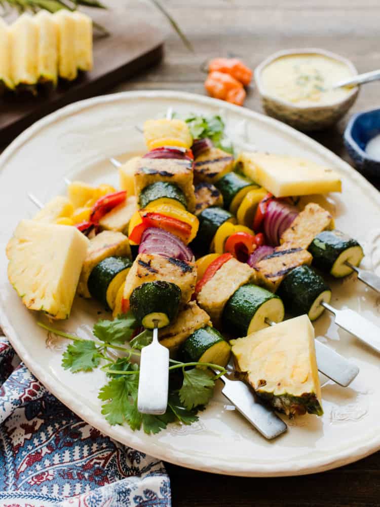 Grilled vegetable skewers with pineapple on a white plate.