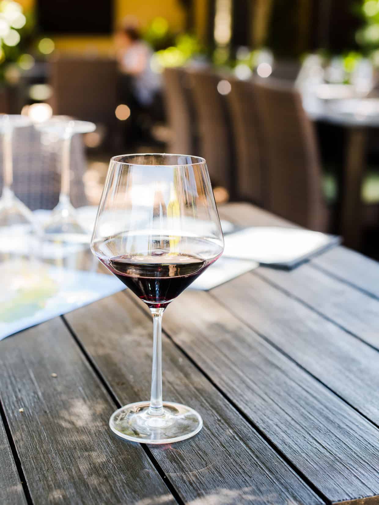 A glass of red wine with tables and chairs in the background.