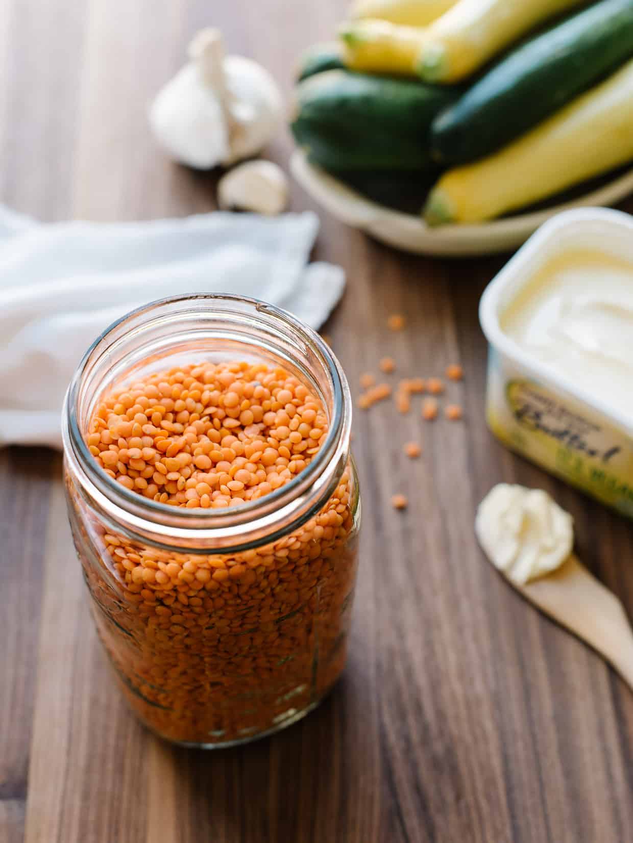 A jar of red lentils with zucchini and summer squash in the background.