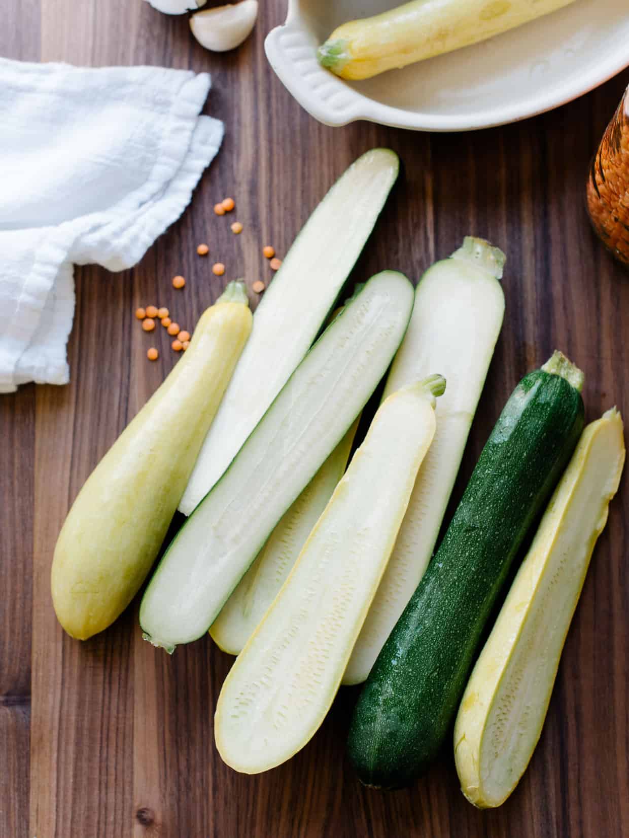 Zucchini and summer squash sliced lengthwise on a wooden cutting board.