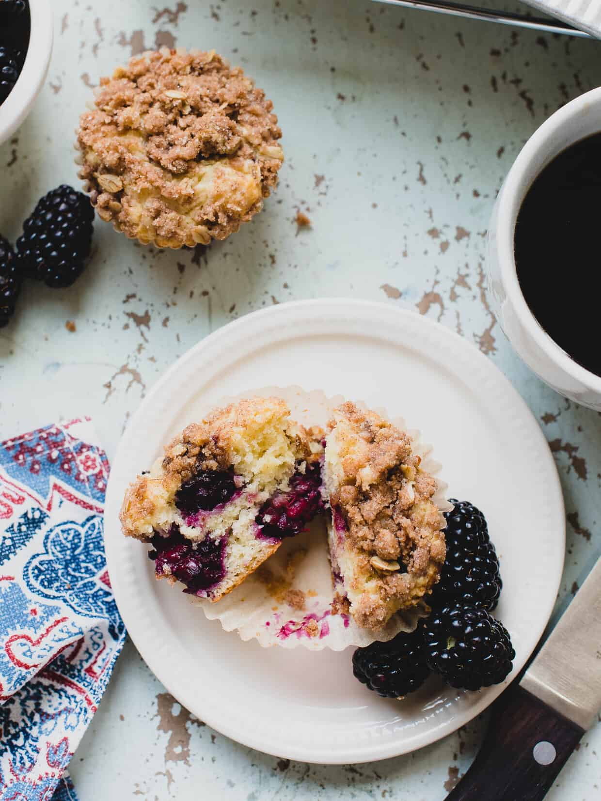 Blackberry Yogurt Muffin cut in half and served on a white plate surrounded by blackberries.
