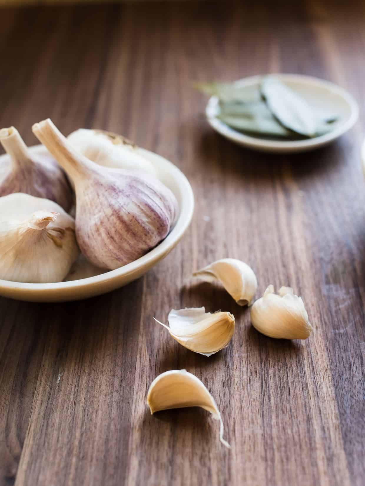 Garlic cloves in a bowl and on a wooden surface.