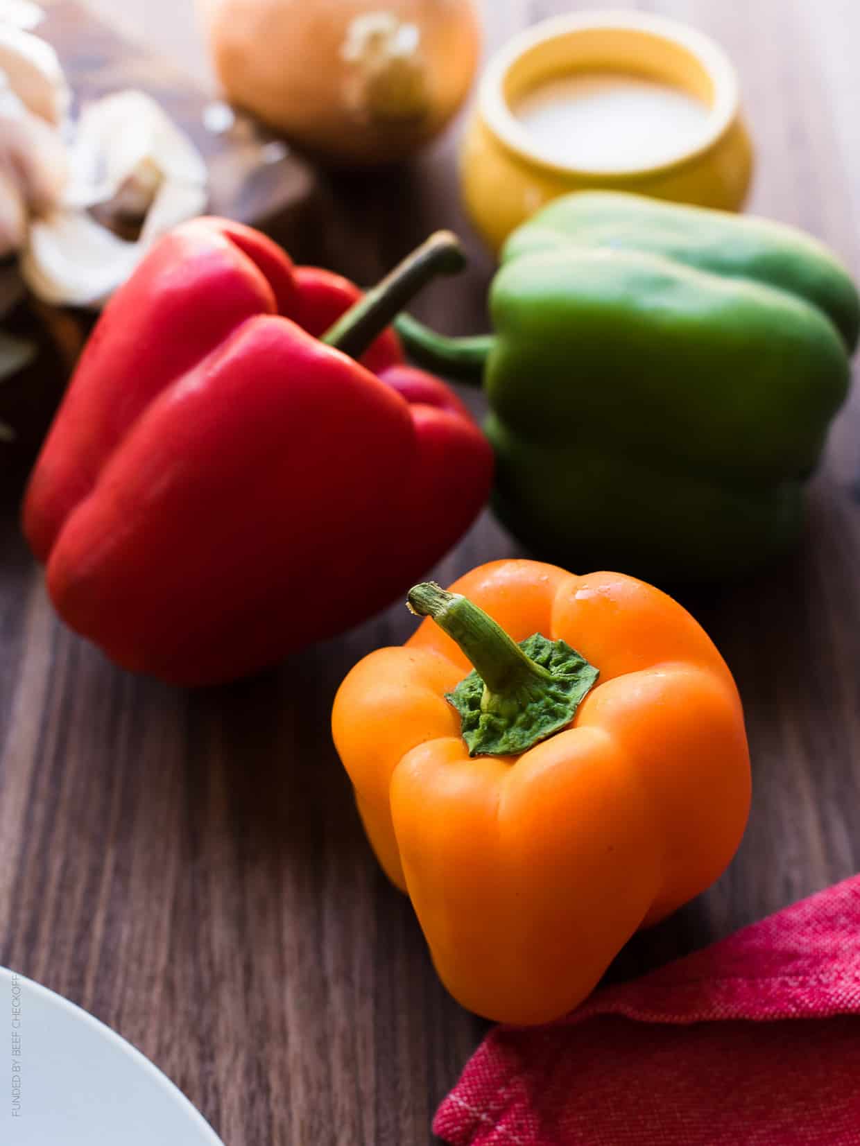 Orange, red, and green bell peppers on a wooden surface.