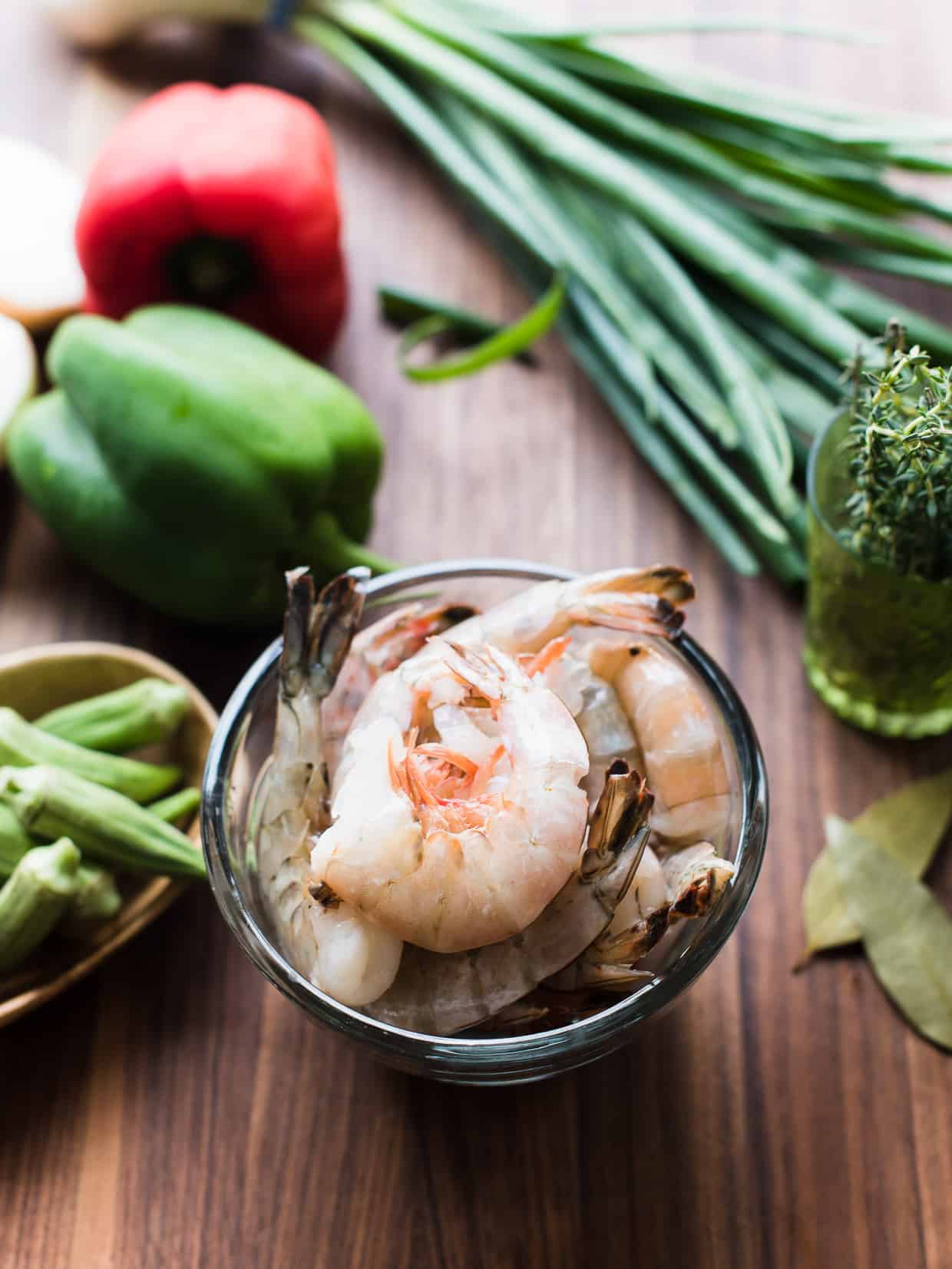 Fresh shrimp surrounded by bell peppers and other ingredients on a wooden surface.