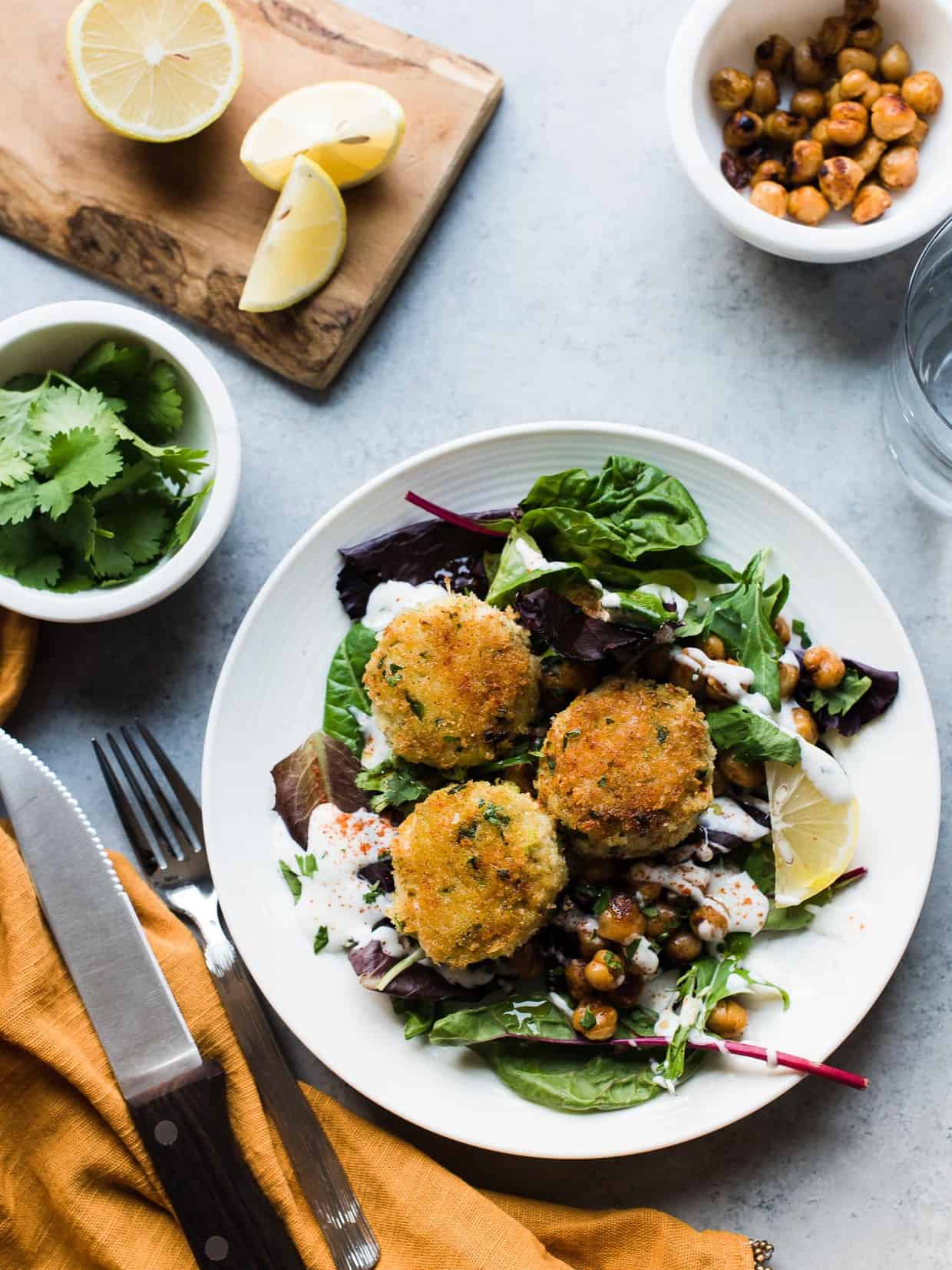 Plate of Chickpea Crab Cakes surrounded by fresh lemon, cilantro, and chickpeas.