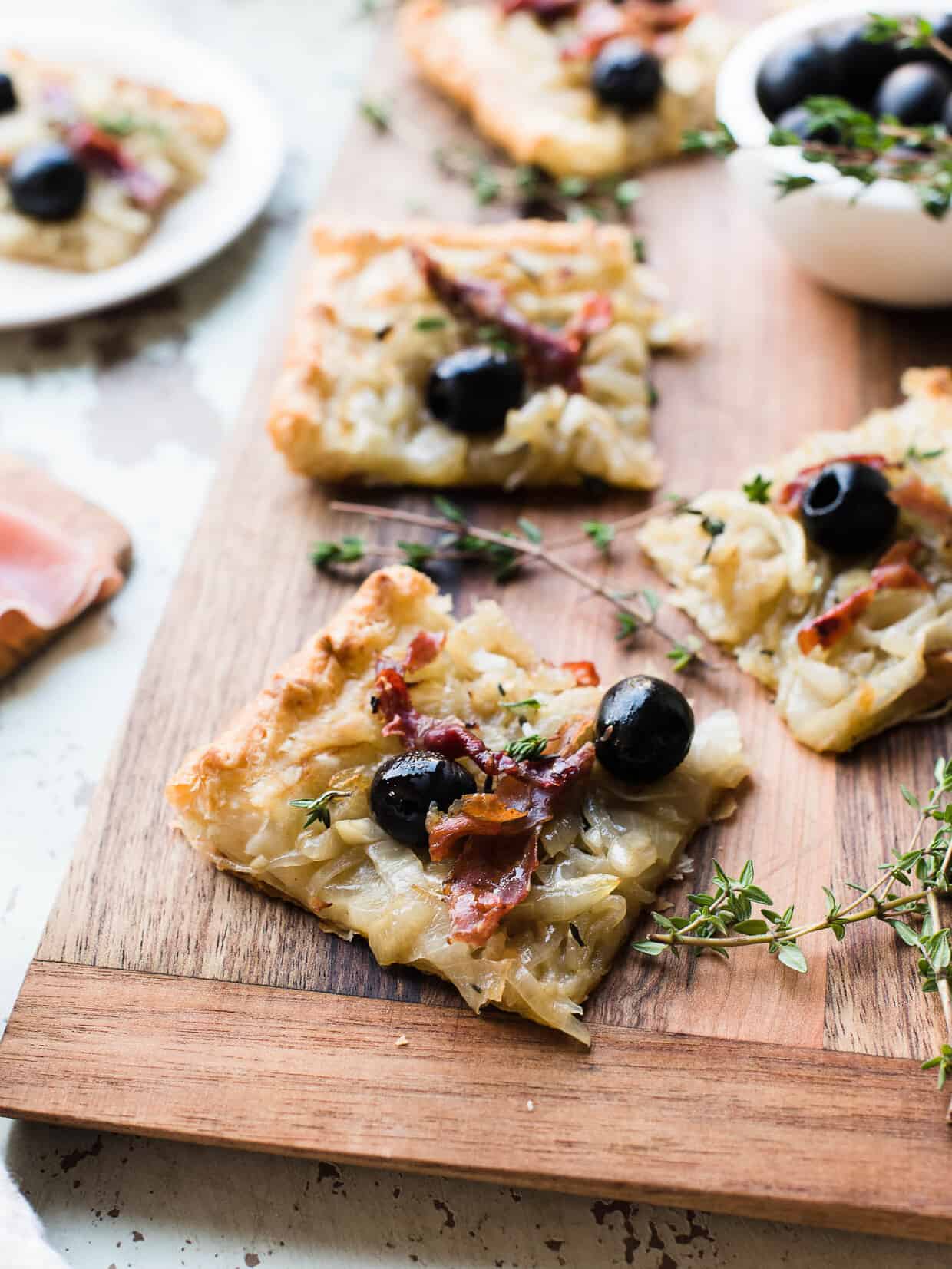 Slices of Pissaladière with Prosciutto on a wooden serving board.