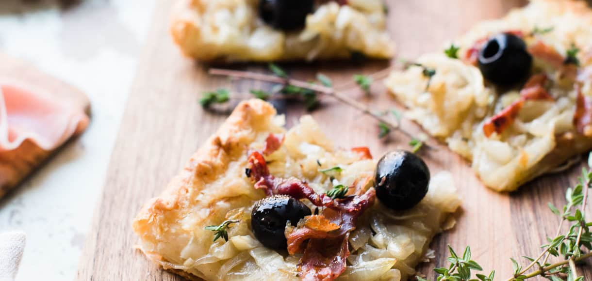 Slices of homemade Pissaladière with Prosciutto on a wooden serving board.