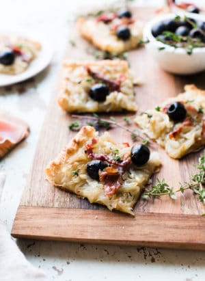 Slices of homemade Pissaladière with Prosciutto on a wooden serving board.